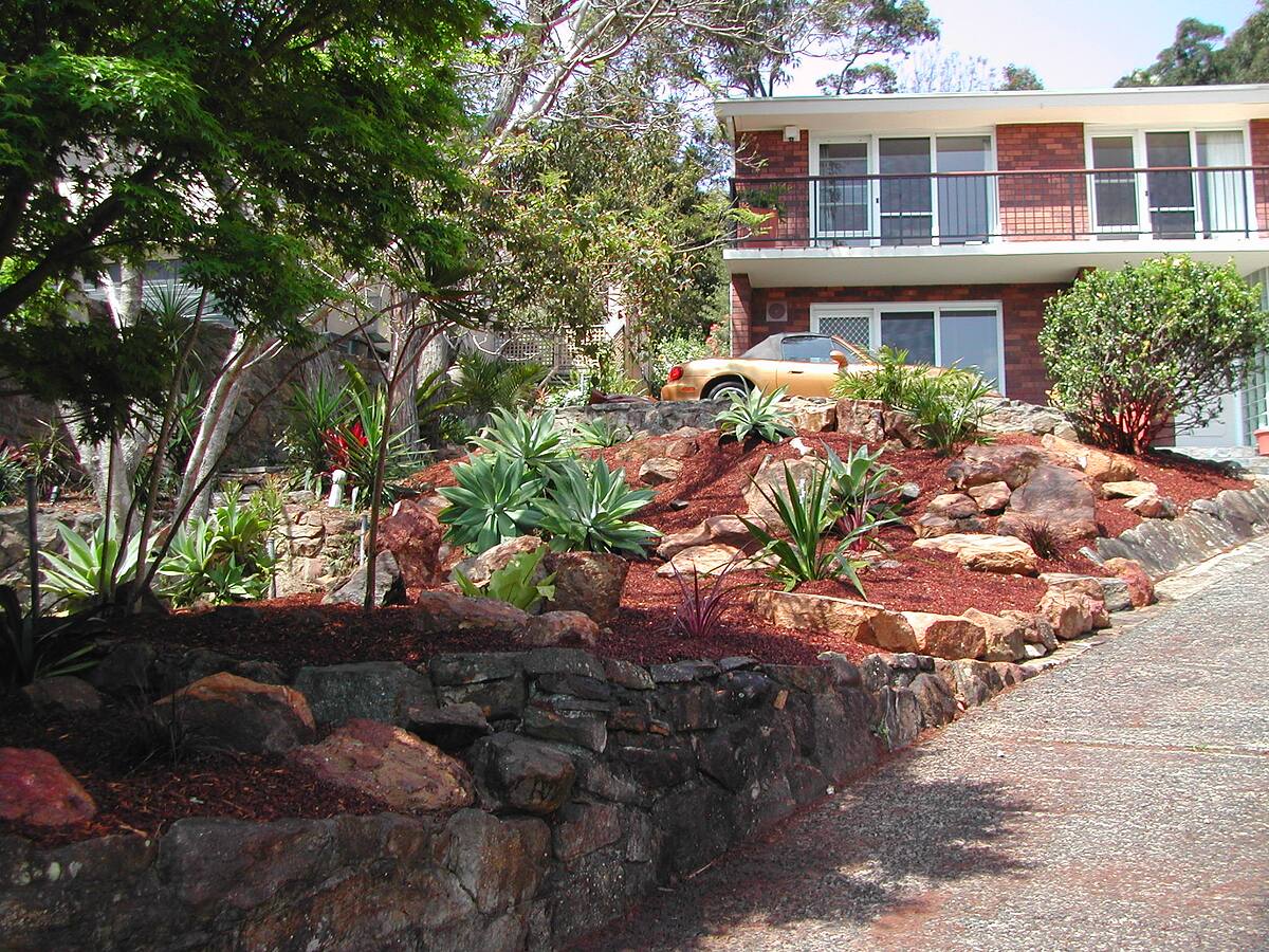 Front garden with sandstone boulders, agaves and red mulch in Cromer